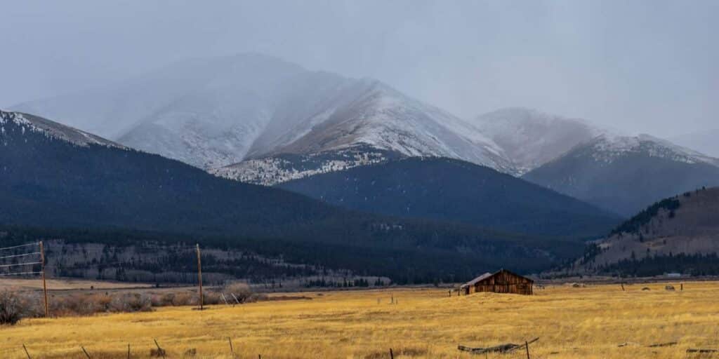 Open rural field with a small home below the mountains in Colorado